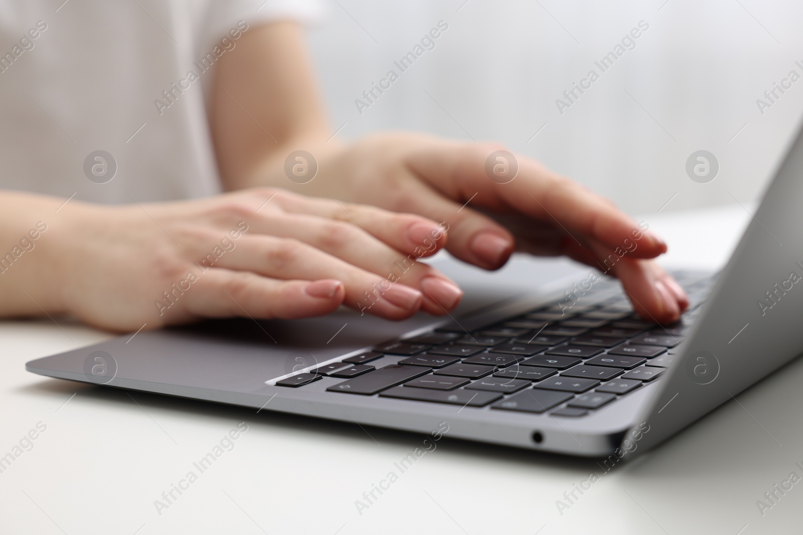 Photo of E-learning. Woman using laptop at white table indoors, closeup