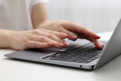 E-learning. Woman using laptop at white table indoors, closeup