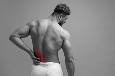 Man suffering from back pain on grey background. Black and white effect with red accent