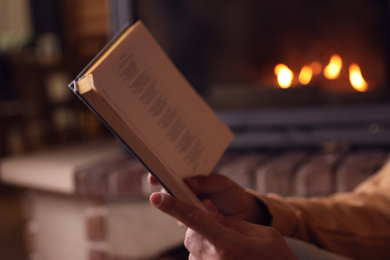 Man reading book near fireplace at home, closeup