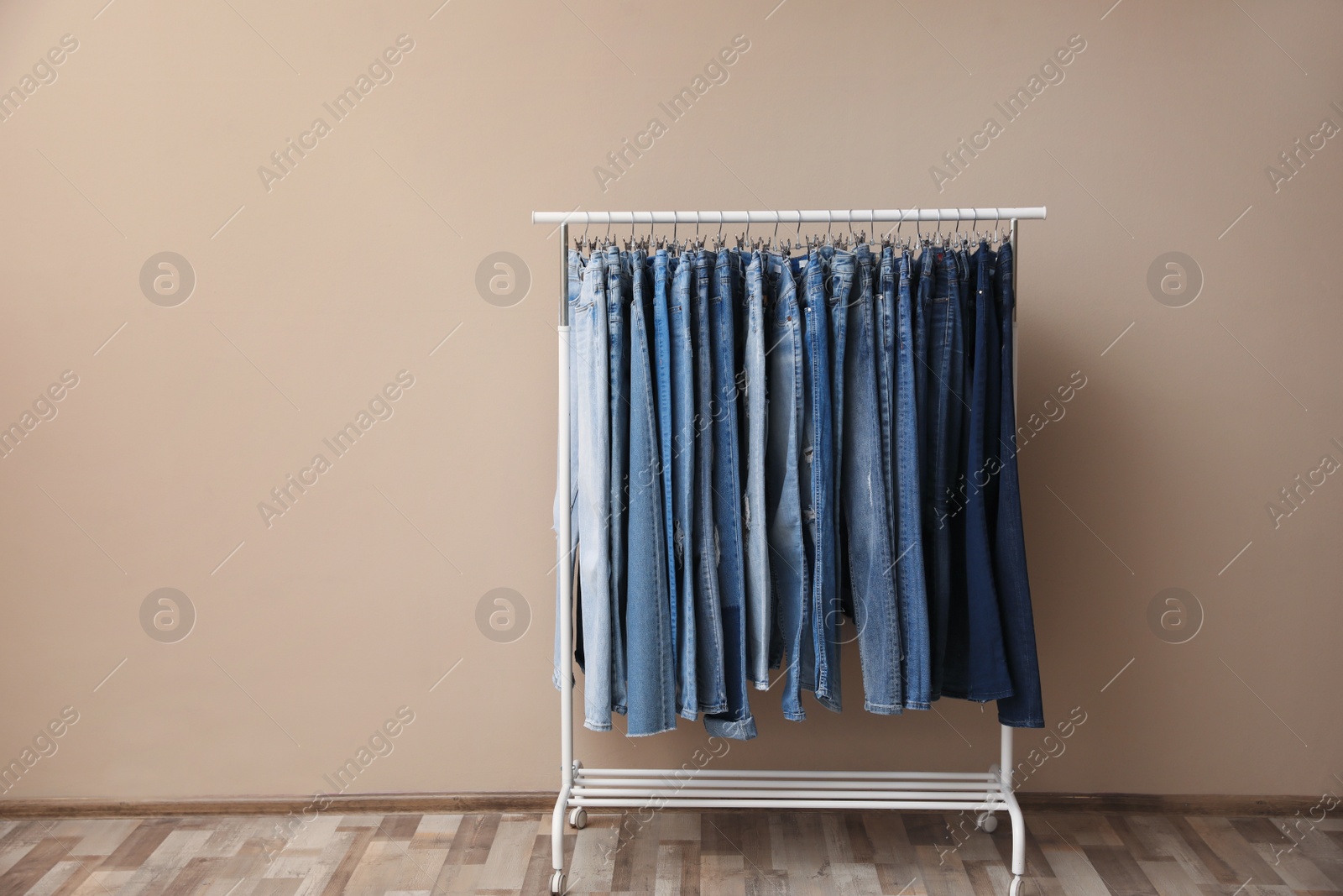 Photo of Rack with stylish jeans on near beige wall