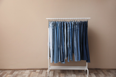 Photo of Rack with stylish jeans on near beige wall