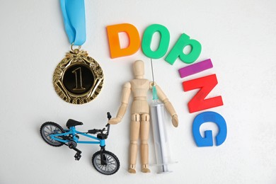 Photo of Word Doping, syringe, medal, sportsman and bicycle model on white table, flat lay