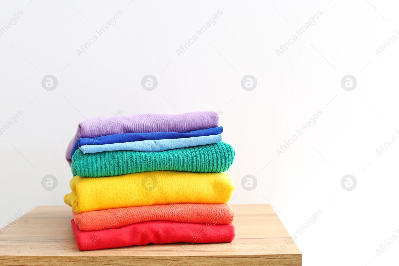 Photo of Stack of rainbow clothes on table against white background