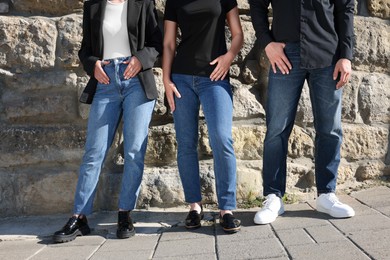 Photo of People in stylish jeans near stone wall outdoors on sunny day, closeup