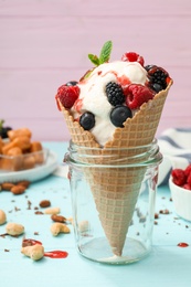 Photo of Delicious ice cream with berries in wafer cone served on light blue table