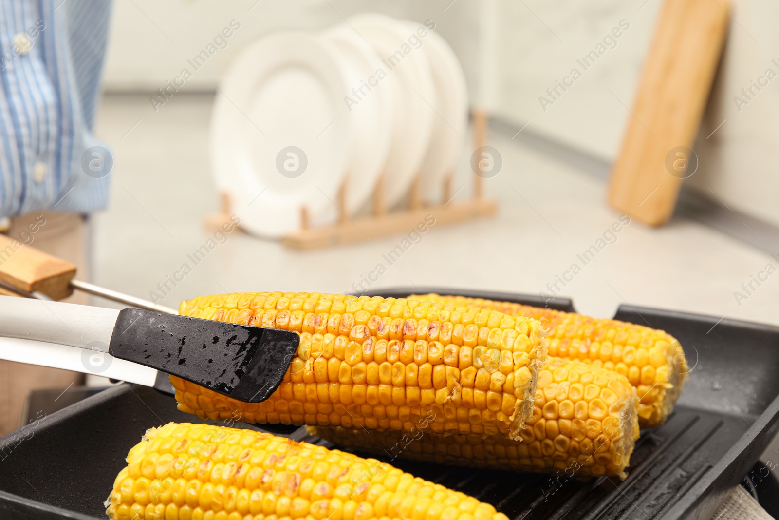 Photo of Taking corn from grill pan with tongs in kitchen, closeup