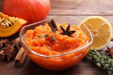 Photo of Bowl of delicious pumpkin jam and ingredients on wooden table, closeup