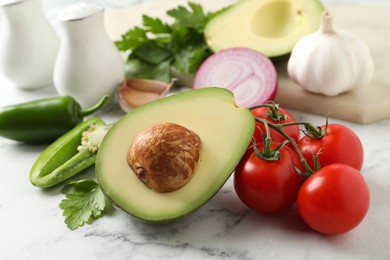 Fresh ingredients for guacamole on white marble table, closeup