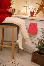 Photo of Woman with cup of hot drink sitting on bar stool in kitchen decorated for Christmas, closeup