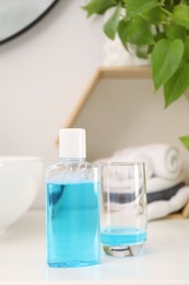 Bottle of mouthwash and glass on white table in bathroom