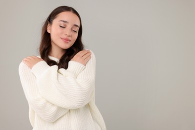 Photo of Beautiful young woman in stylish warm sweater on grey background, space for text