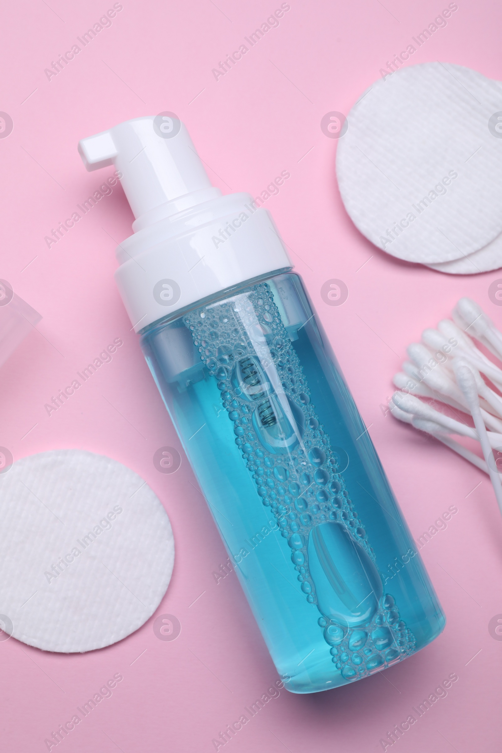 Photo of Bottle of face cleansing product, cotton buds and pads on pink background, flat lay. Space for text