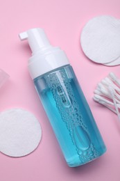 Photo of Bottle of face cleansing product, cotton buds and pads on pink background, flat lay. Space for text