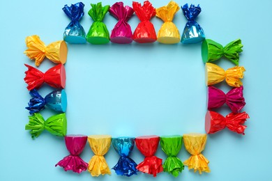 Photo of Frame of candies in colorful wrappers on light blue background, flat lay. Space for text