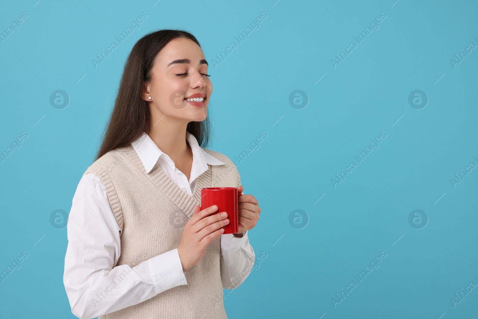 Photo of Happy young woman holding red ceramic mug on light blue background, space for text