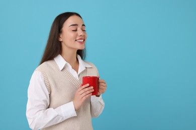 Happy young woman holding red ceramic mug on light blue background, space for text