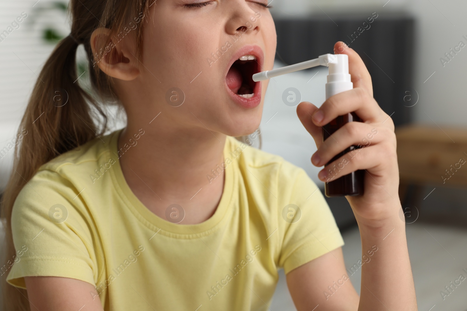 Photo of Little girl using throat spray at home, closeup