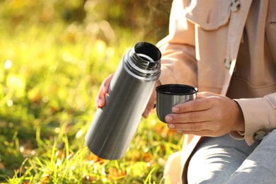 Photo of Woman with thermos and cup lid on green grass outdoors, closeup. Space for text