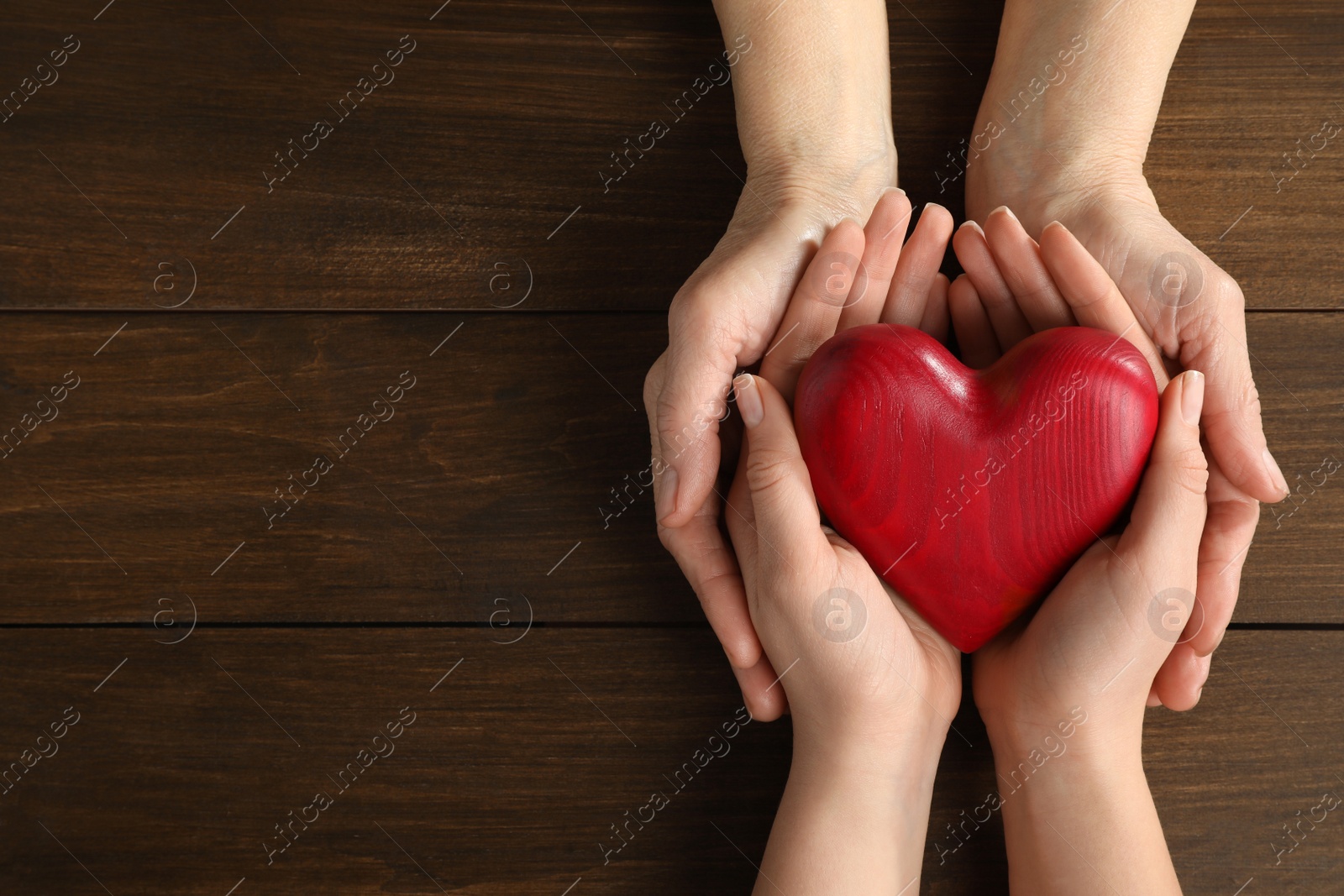 Photo of Young and elderly women holding red heart at wooden table, top view. Space for text