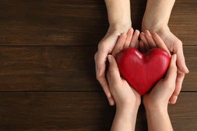 Young and elderly women holding red heart at wooden table, top view. Space for text