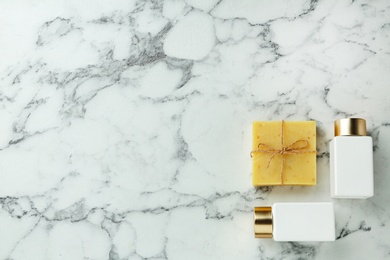 Photo of Cosmetic bottles and handmade soap on marble table, flat lay with space for text. Spa treatment