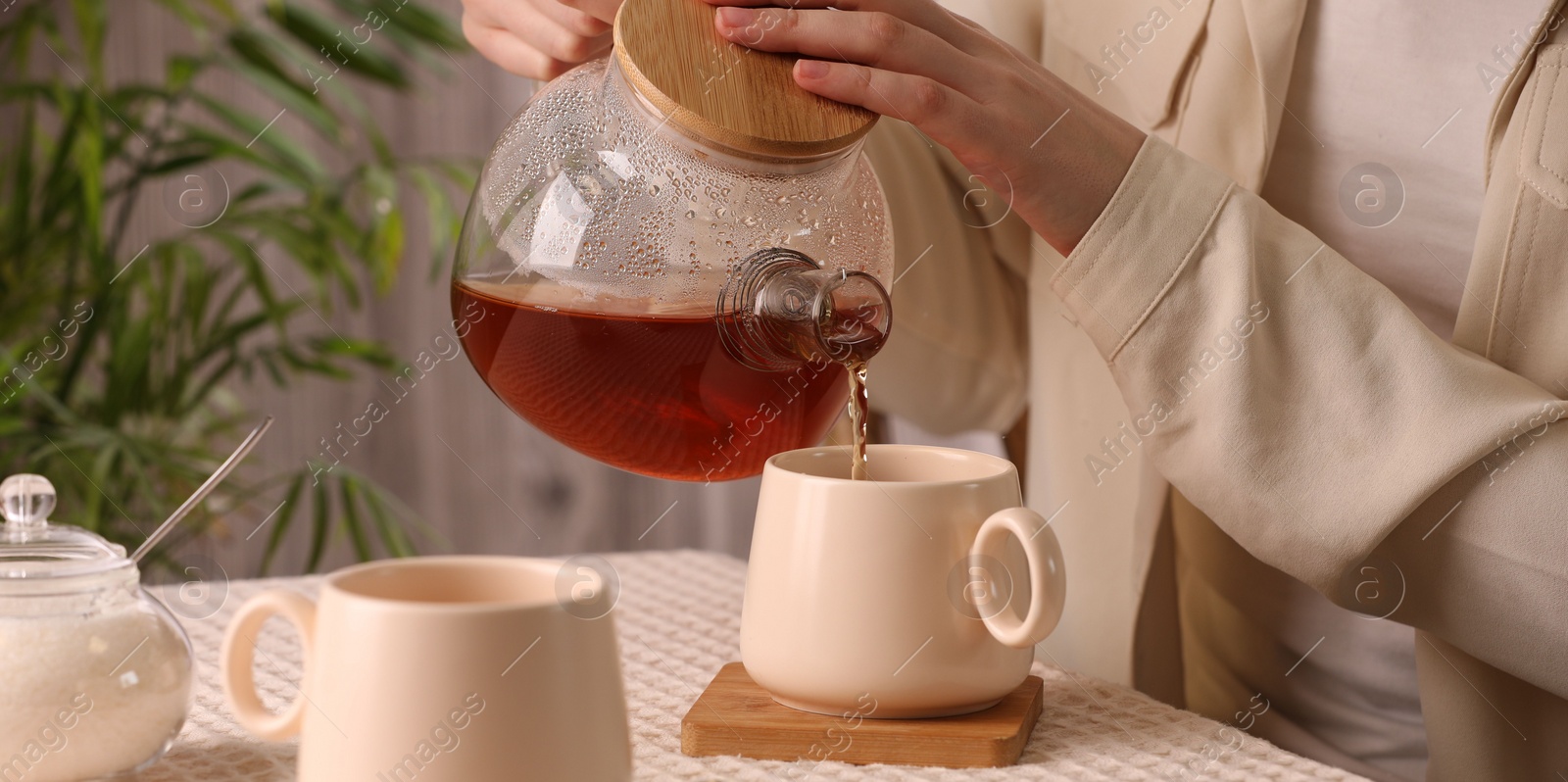 Photo of Woman pouring aromatic tea into cup at table, closeup