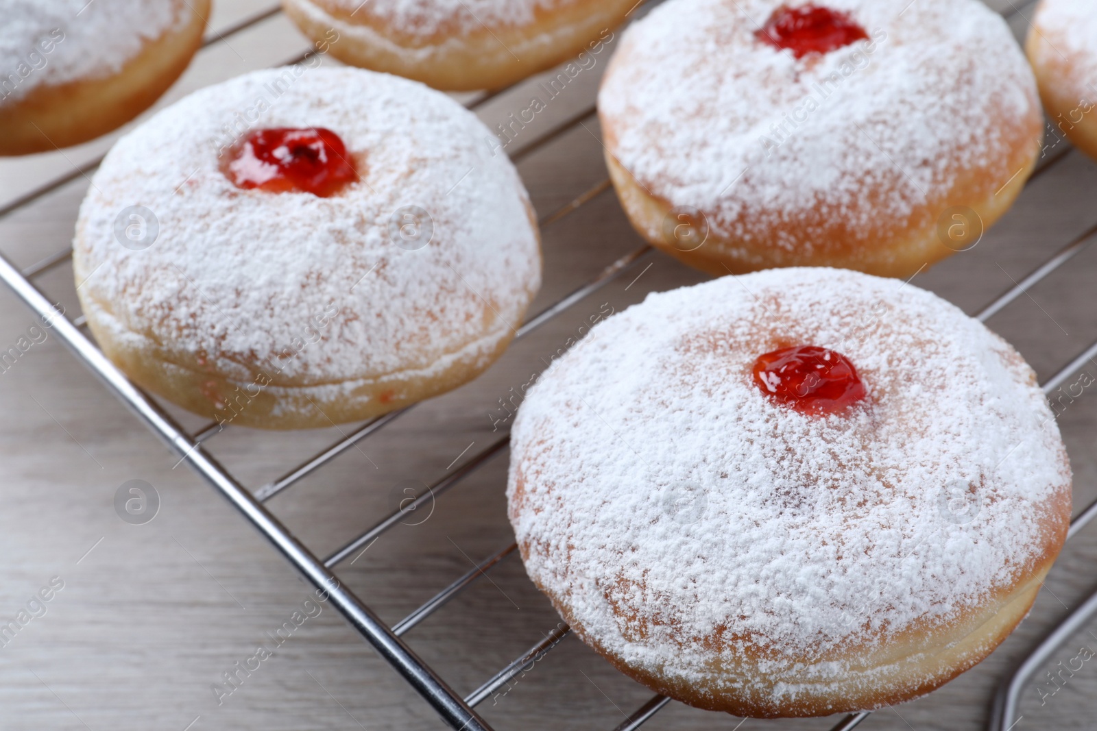 Photo of Many delicious donuts with jelly and powdered sugar on cooling rack, closeup