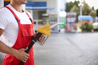 Worker with fuel pump nozzle at modern gas station, closeup