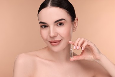 Photo of Beautiful young woman holding skincare ampoule on beige background