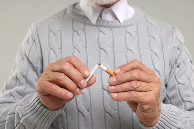 Stop smoking concept. Man breaking cigarette on light grey background, closeup