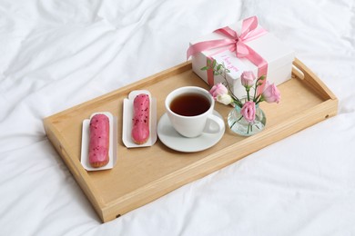 Photo of Tasty breakfast served in bed. Delicious eclairs, tea, gift box, flowers and card with phrase I Love You on tray