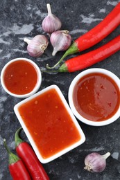 Photo of Spicy chili sauce, peppers and garlic on black textured table, flat lay