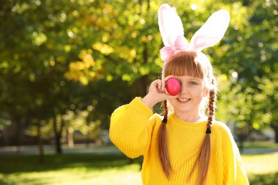 Photo of Cute little girl with bunny ears holding Easter egg in park. Space for text