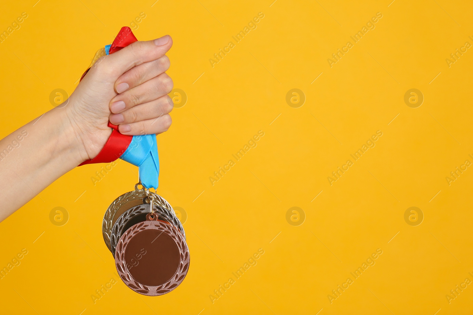 Photo of Woman holding medals on yellow background, closeup. Space for design