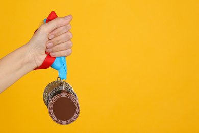 Woman holding medals on yellow background, closeup. Space for design