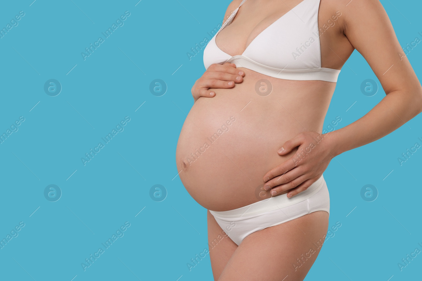 Photo of Pregnant woman in stylish comfortable underwear on light blue background, closeup. Space for text