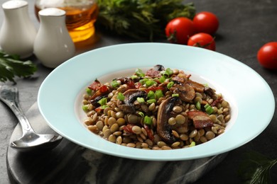 Photo of Delicious lentils with mushrooms, bacon and green onion on grey table, closeup