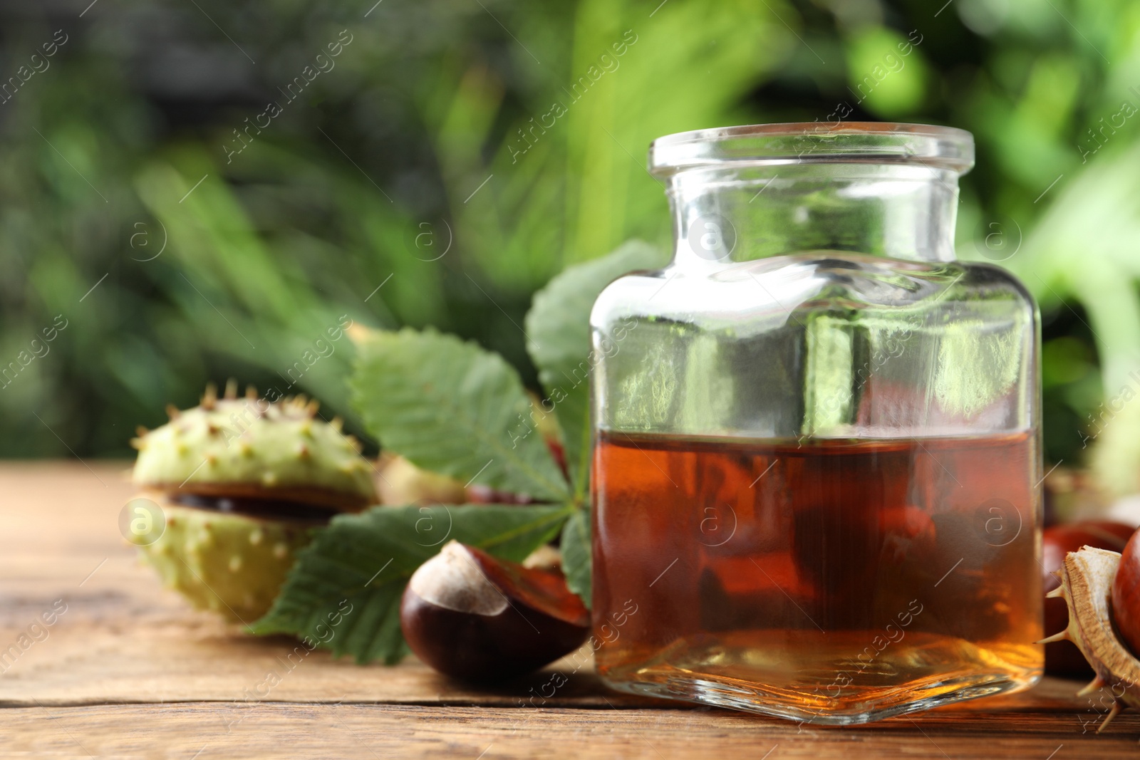 Photo of Chestnuts and jar of essential oil on table against blurred background. Space for text