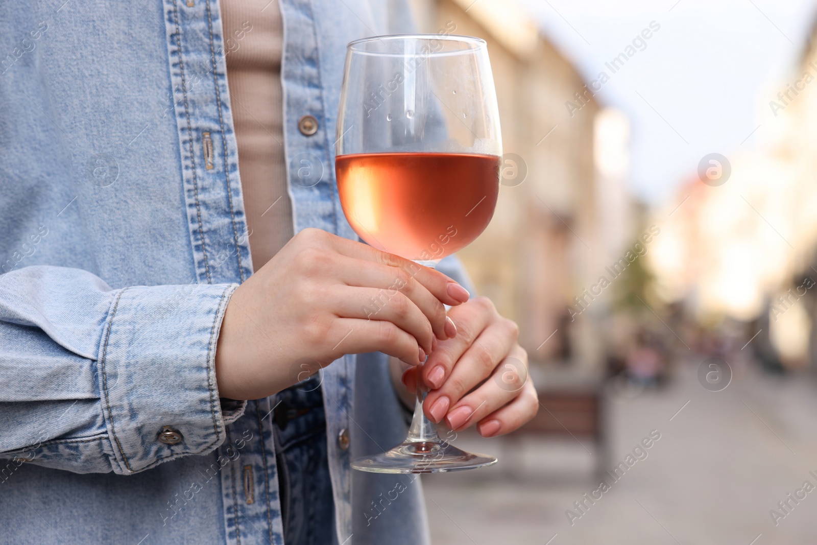 Photo of Woman holding glass of rose wine outdoors, closeup. Space for text