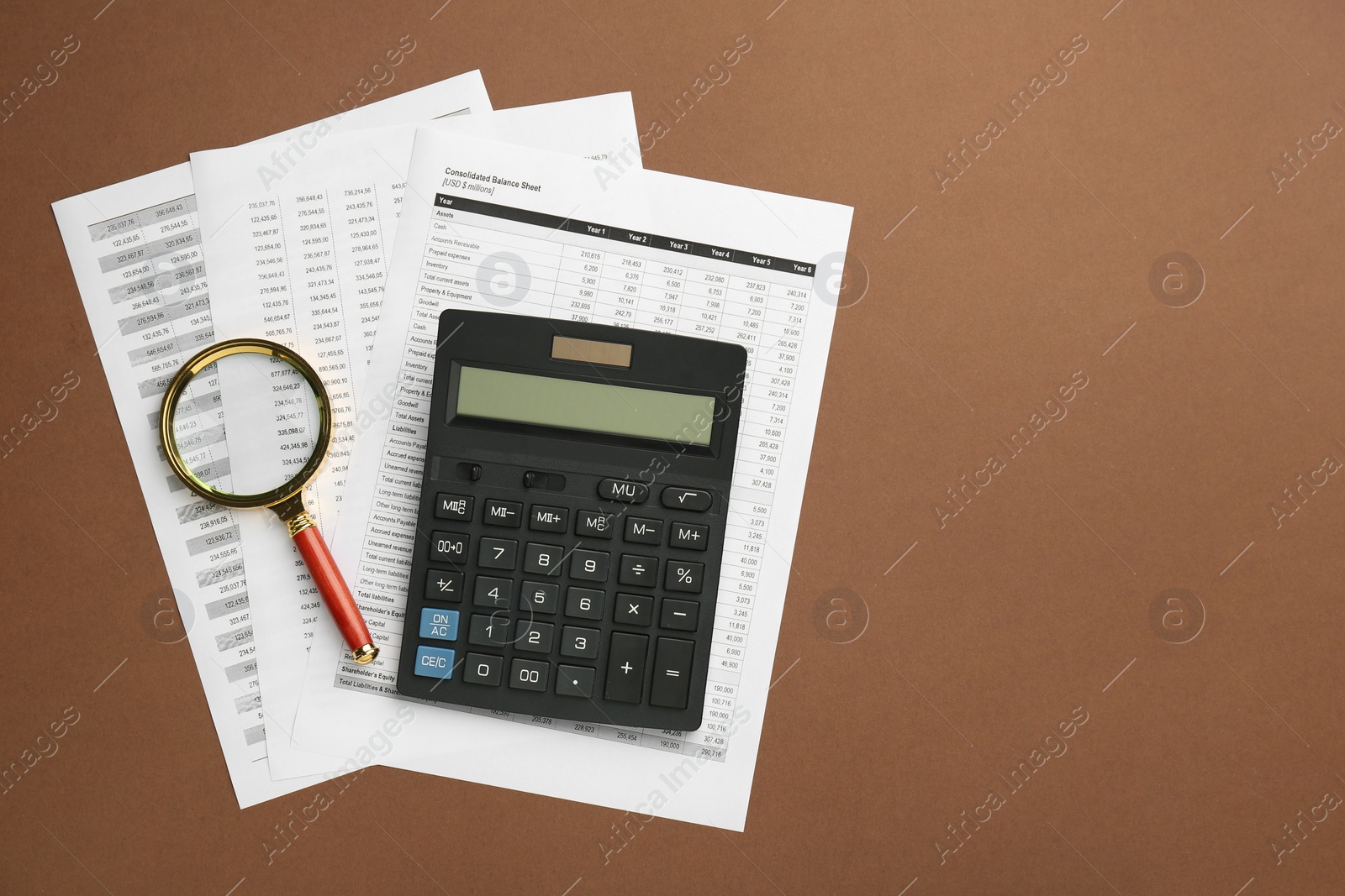 Photo of Accounting documents, magnifying glass and calculator on brown background, top view. Space for text