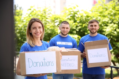 Photo of Young volunteers holding boxes with donations for poor people outdoors