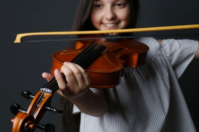 Photo of Preteen girl playing violin on black background, closeup