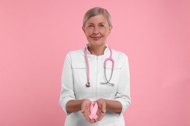 Photo of Doctor with stethoscope holding pink ribbon on color background. Breast cancer awareness