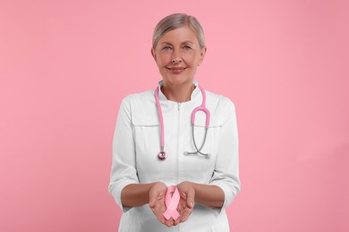 Doctor with stethoscope holding pink ribbon on color background. Breast cancer awareness