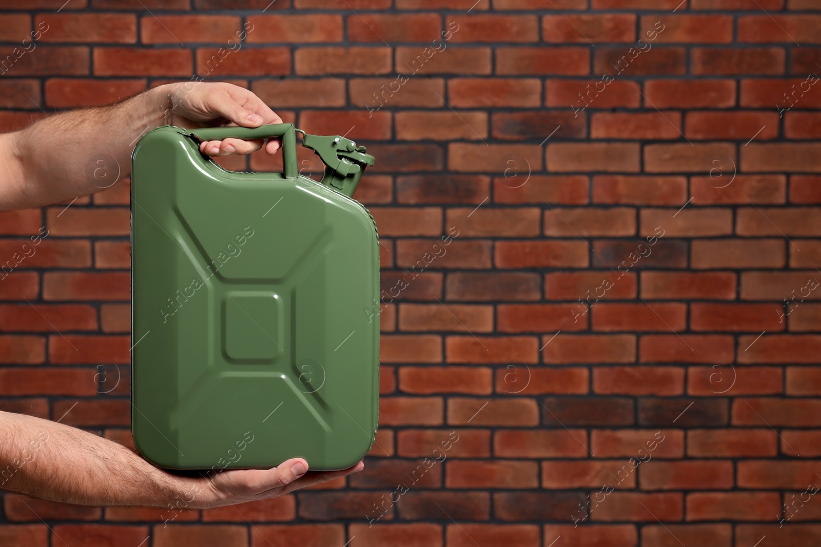 Photo of Man holding khaki metal canister against brick wall, closeup. Space for text