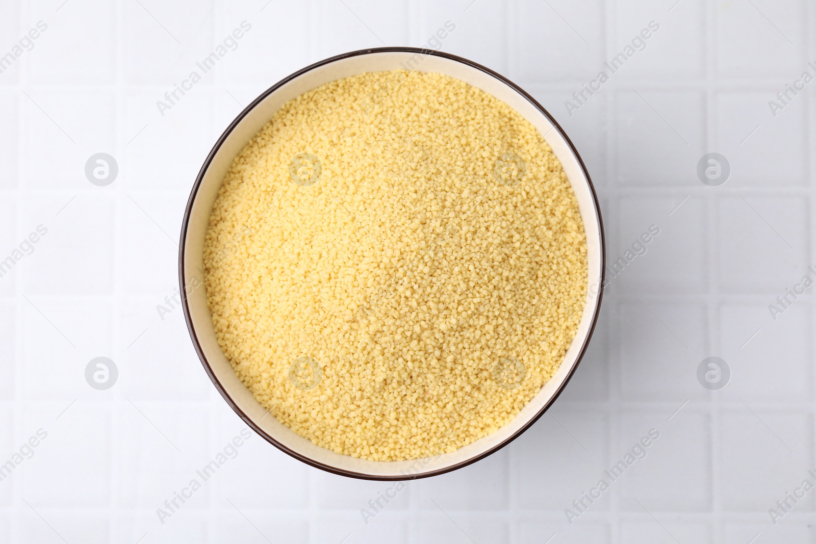 Photo of Raw couscous in bowl on white tiled table, top view