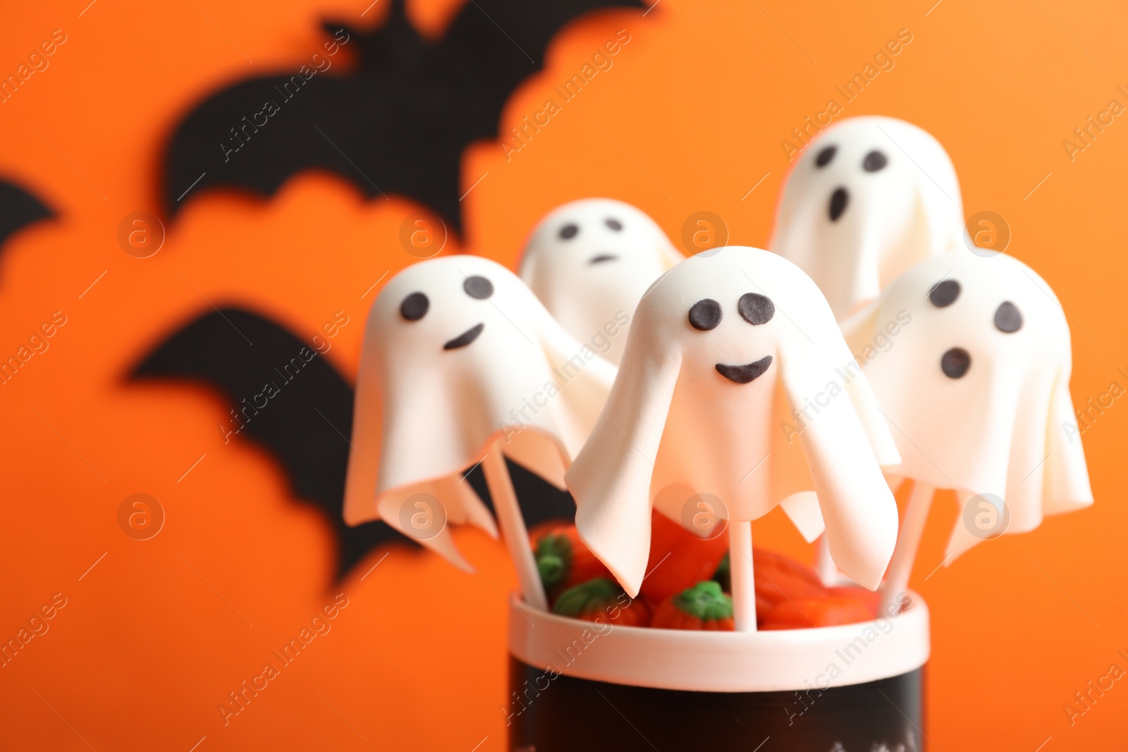 Photo of Delicious ghost shaped cake pops on orange background, closeup. Halloween celebration