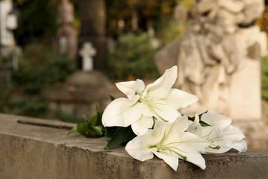 Photo of White lilies on grey tombstone outdoors, space for text . Funeral ceremony