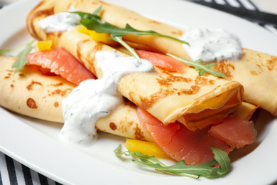 Photo of Delicious thin pancakes with salmon and sour cream on plate, closeup